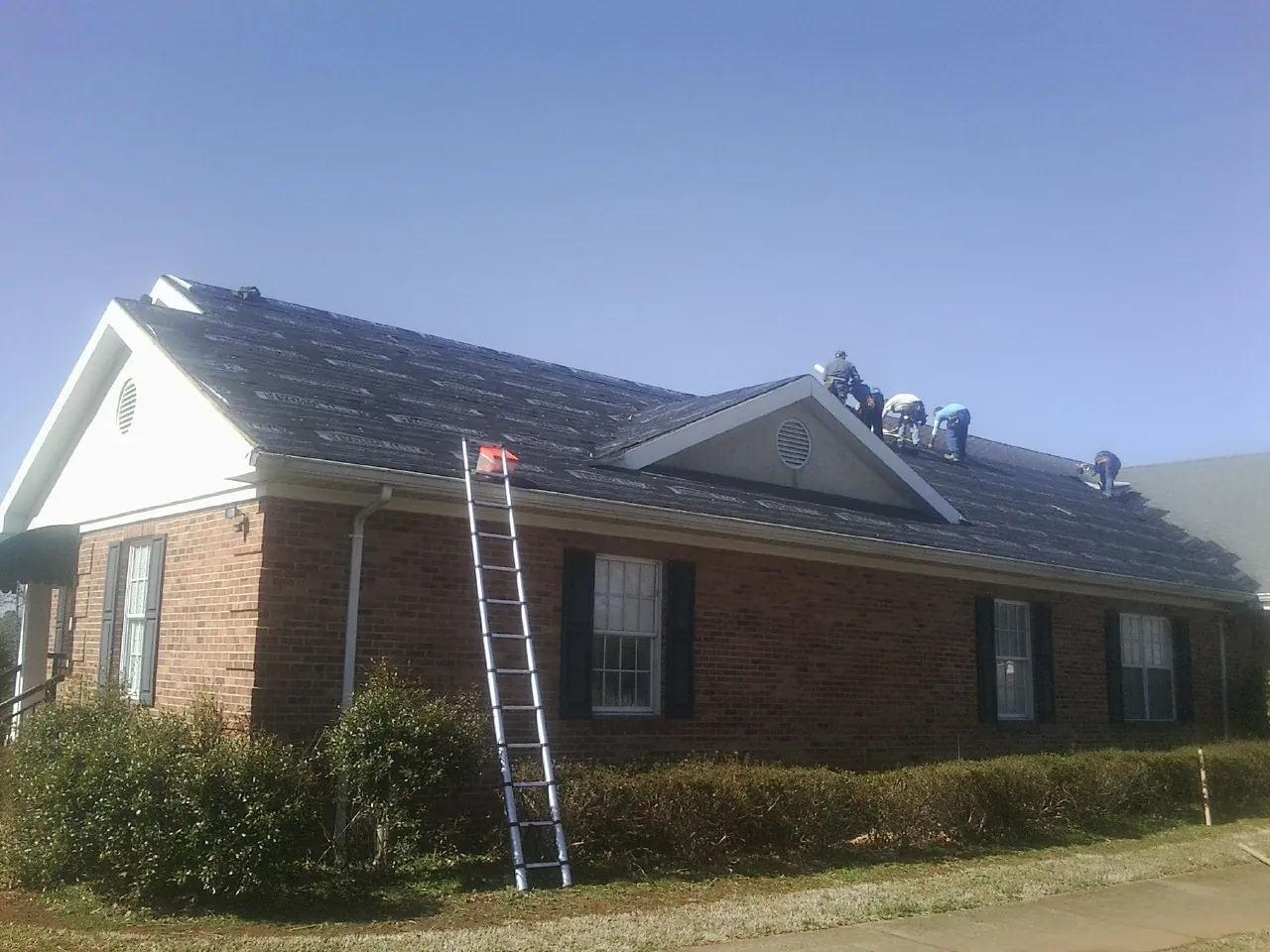 Crew tearing shingles off a brick ranch roof with a ladder set — Emergency Roof Repair work by our crew in Lockhart