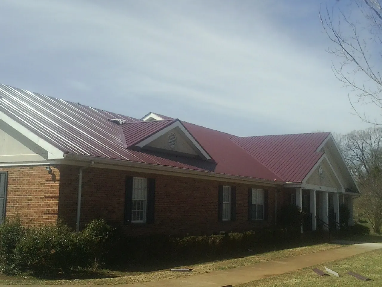 Red metal roof with gabled entries on a long brick building, from a Hail Damage Roof Repair job in Lockhart