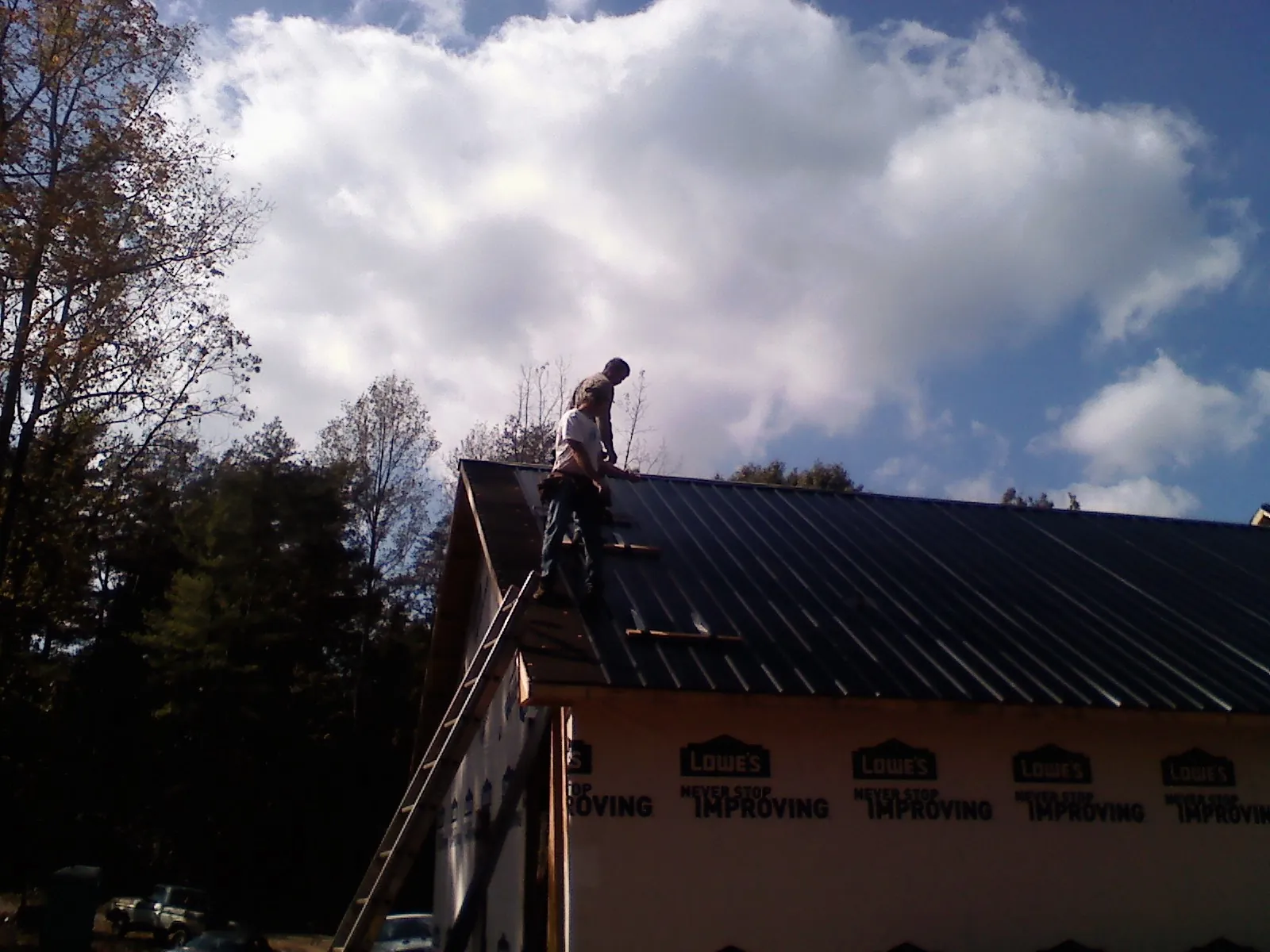 Roofer fastening dark metal panels high against a cloudy sky, from a Roof Inspection job in Lockhart